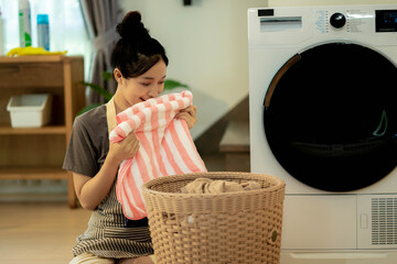 Feel softness, smiling asian young woman is smiling while doing laundry at home.