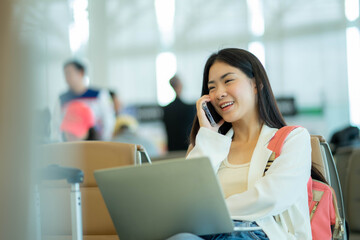 Asian woman sitting at the airport terminal departure lounge and talking on the cell phone while waiting for a flight. Travel concept.