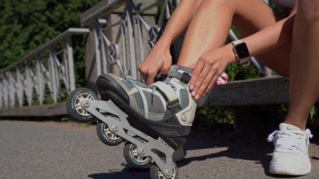 Close-up girl putting on inline skates rollers in public park in summer. Youth leisure outdoor sport activity game pursuit, hobby, healthy lifestyle.