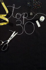 Sewing theme, 30 best written and embroidered on a black fabric with sewing accessories, top view