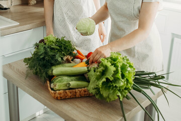 A woman puts various vegetables on the kitchen table for preparing dietary food.