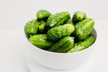 Green cucumbers in a white plate on a white background.