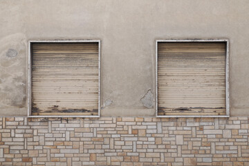 Two old window with rolled up jalousie on cracked cement wall with brick  tiles