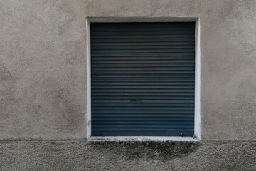 Grey old house wall with dark aluminium shutter, jalousie rolled up