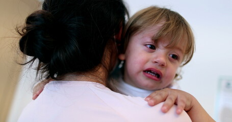 Fototapeta na wymiar Tearful baby boy. Mother wearing surgical mask holding upset crying infant