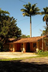 Fototapeta na wymiar Casa com varanda, paredes de tijolo a vista, talhado de telha de barro e muitas árvores no jardim.