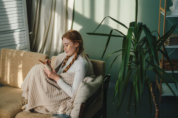 Beautiful woman sitting on sofa in cozy sweater and writing in notebook. Holidays and leisure...