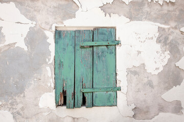 Damaged and cracked house wall with window and green closed wooden shutter, no person