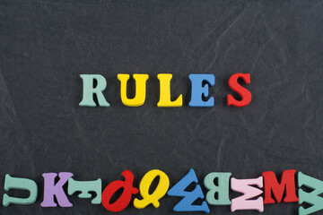 Obraz premium RULES word on black board background composed from colorful abc alphabet block wooden letters, copy space for ad text. Learning english concept.