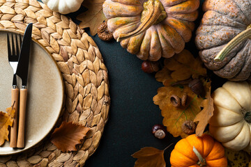 Cozy hygge table. Top view of plate and cutlery, pumpkins, autumn leaves on dark table. Autumn table setting. Festive Thanksgiving or Halloween background. Restaurant menu. Copy space
