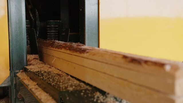 Industrial sawmill machinery processing logs into wooden boards. A toothed feeding mechanism moves a log through the cutting machine, producing lumber during timber processing.