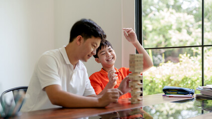 Father and son play board games and pull out wooden block from tower with family activity at home