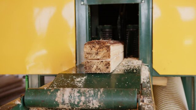 Industrial sawmill machinery processing logs into wooden boards. A toothed feeding mechanism moves a log through the cutting machine, producing lumber during timber processing.