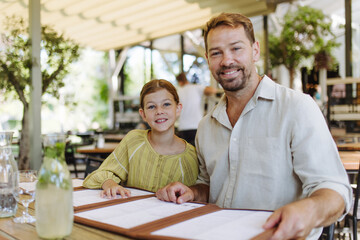 Father and daughter reading menus in a restaurant, choosing food and drinks.