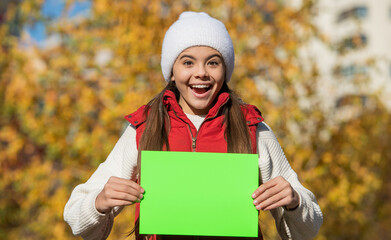 autumn sale ad. teenage girl with autumn advertising, copy space. teenage girl in autumn with paper. girl hold blank paper for advertisement outdoor. fall season for school time