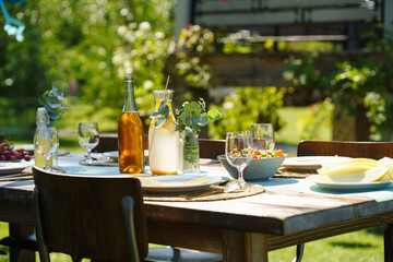 Close up of set table at summer garden party. Table setting with glasses, lemonade, fresh fruits and salad and delicate floral decoration.