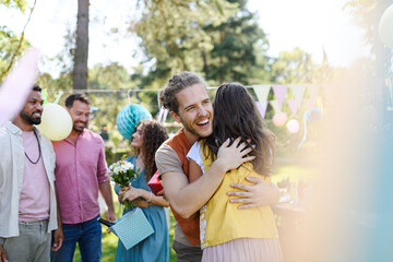 Friends reunite after a long time apart. Men and women embracing, happy to meet at garden party.