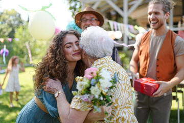 Garden birthday party for senior lady. Beautiful senior birthday woman hugging granddaughter.