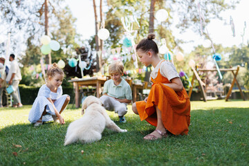 Children playing with a small puppy at a family garden party. Family gathering outdoors during warm...