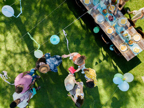 Top view of a garden party with decorations and set table. The birthday girl greeting guests and receiving birthday wishes and gifts.