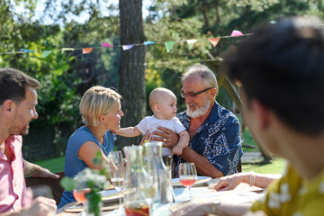 Cute baby playing with grandfather at summer garden party. The grandfather holding baby boy in his...