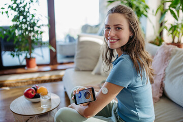 Woman with diabetes using continuous glucose monitor. Diabetic woman connecting CGM to smartphone to monitor her blood sugar levels in real time. - obrazy, fototapety, plakaty