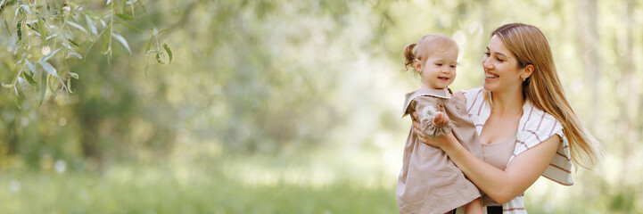 A young european woman in casual, comfortable beige clothes holding a small child in her arms in...