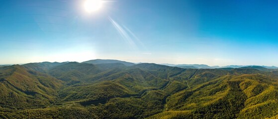 a typical view of the not very high mountains of the Western Caucasus, covered with green deciduous forest on a sunny day in early autumn - aerial panorama
