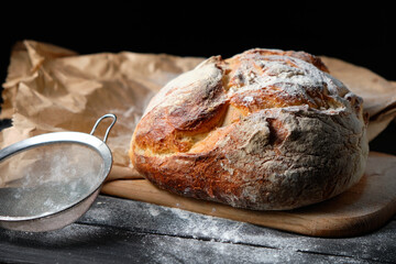 fresh loaf of bread sprinkled with flour on a wooden background