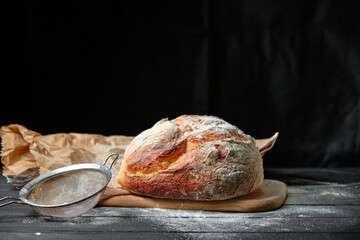 fresh loaf of bread sprinkled with flour on a wooden background