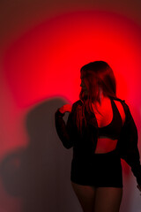 Beautiful young model wearing black clothes posing for photo illuminated in red color.