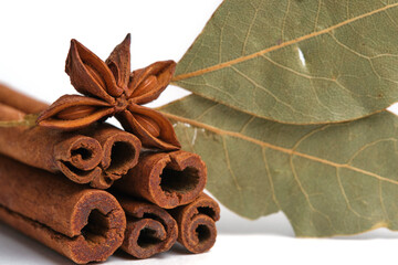 Spicy spices cinnamon sticks and star anise with bay leaf on white background.