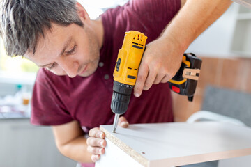 Professional carpenter working with electric cordless screwdriver. Kitchen installation concept.