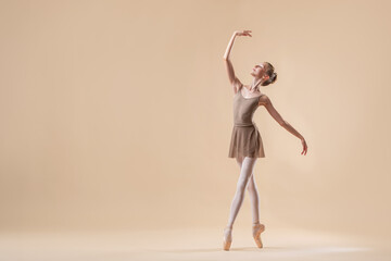 Beautiful young girl professional student ballerina in pointe shoes and a leotard on a light beige...