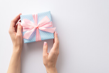 A special moment captured from first person top view: my hands demonstrate a pastel blue gift box with polka dots and a sweet pink ribbon bow. Create your message against the blank white background
