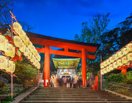 kanagawa, enoshima - dec 25 2022: Low angle of the stairs lined with lit paper lanterns lined up leading to Enoshima Shrine's torii gate and gold-leafed Zuishinmon gate crowded with tourists at dusk.