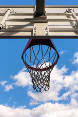 ?A basketball hoop with a net on a court against a backdrop of blue skies and fluffy white clouds, offering the perfect setting for outdoor sports and recreation.