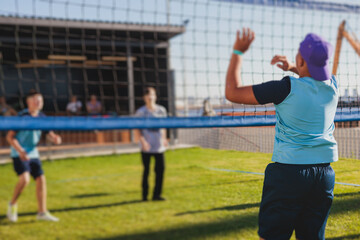 Volleyball game, junior teenage school team of kids play volleyball, players on the outdoor playground with net and green lawn grass court, sports children team during the game, summer sunny
