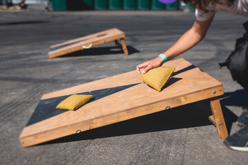 Cornhole game set, process of throwing bean bags, kids children tossing bean sacks, corn hole  in the backyard, wooden boards for corn-hole tournament in the summer sunny day - obrazy, fototapety, plakaty