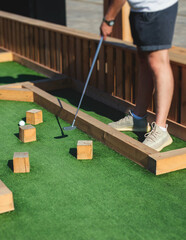 Mini golf course, process of playing miniature golf on a green artificial turf in a summer sunny day, eqipment for mini-golf in a golf club resort, club and ball