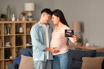 Expectant asian parents hugging showing ultrasound image at home