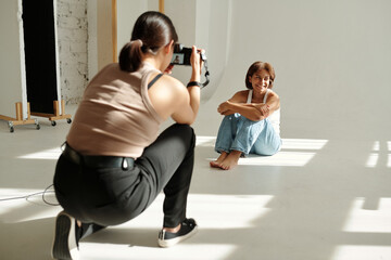 Happy African American girl in casualwear posing for camera while sitting on the floor by wall in...