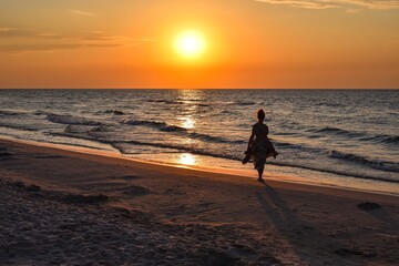 Woman on the seashore in a beautiful evening scenery. Girl walking on the beach with the setting sun in the background. Photo taken at the Baltic Sea in Leba, Poland. - 660144361