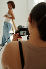 Photocamera held by professional photographer with shot of young female fashion model posing in studio during photo session
