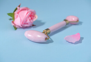 Massage roller for the face made of rose quartz. Gua sha tool for facial massage and age-related skin care. Blue background.