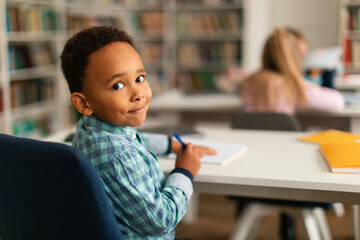 Smiling african american boy in class turning back towards camera - obrazy, fototapety, plakaty