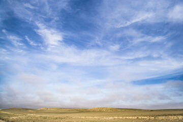 Saturated blue and blue sky with clouds of different shapes in the steppe, minimalistic landscape in the desert