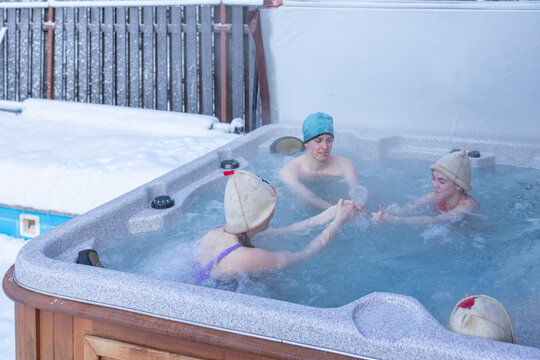 Cheerful happy company of teenagers enjoys hot bath in jacuzzi on cold winter day. Carefree relaxation in hot tub outdoors of nature. Meeting and chatting with friends. High quality photo