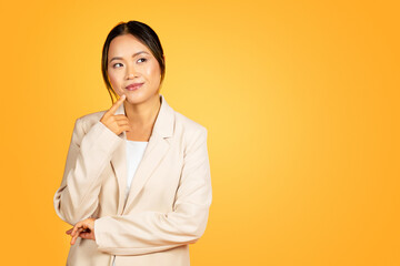 Pensive young Asian woman deep in thought, isolated on yellow studio