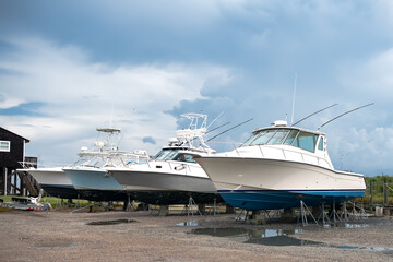 Motor boats stand on land under the open blue sky in the parking lot at the pier.